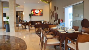 Un espace repas moderne avec plusieurs tables et chaises, un écran de télévision affichant un menu et un extincteur fixé au mur.