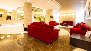 Un hall d’hôtel avec un comptoir d’accueil, des canapés rouges, une table basse et un grand miroir.