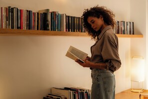 A person reading a book in a room with a bookshelf filled with various books. - 9Hotel Republique (Paris)