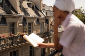 A person reading a book on a balcony with a view of a row of buildings. - 9Hotel Republique (Paris)