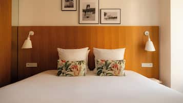 A hotel room with a wooden headboard, two white pillows with floral patterns, and three framed photographs on the wall.