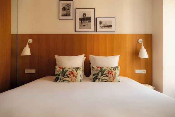 A hotel room with a wooden headboard, two white pillows with floral patterns, and three framed photographs on the wall. - 9Hotel Republique (Paris)