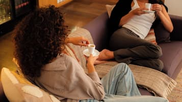 Two people sitting on a sofa with a cup of coffee, in a room with a wooden floor and a television in the background.