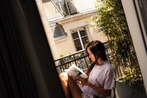 A person sitting on a balcony with a view of a building and some plants.