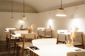 A dining area with white tables and chairs, overhead lighting, and decorative vases with dried flowers. - 9Hotel Republique (Paris)