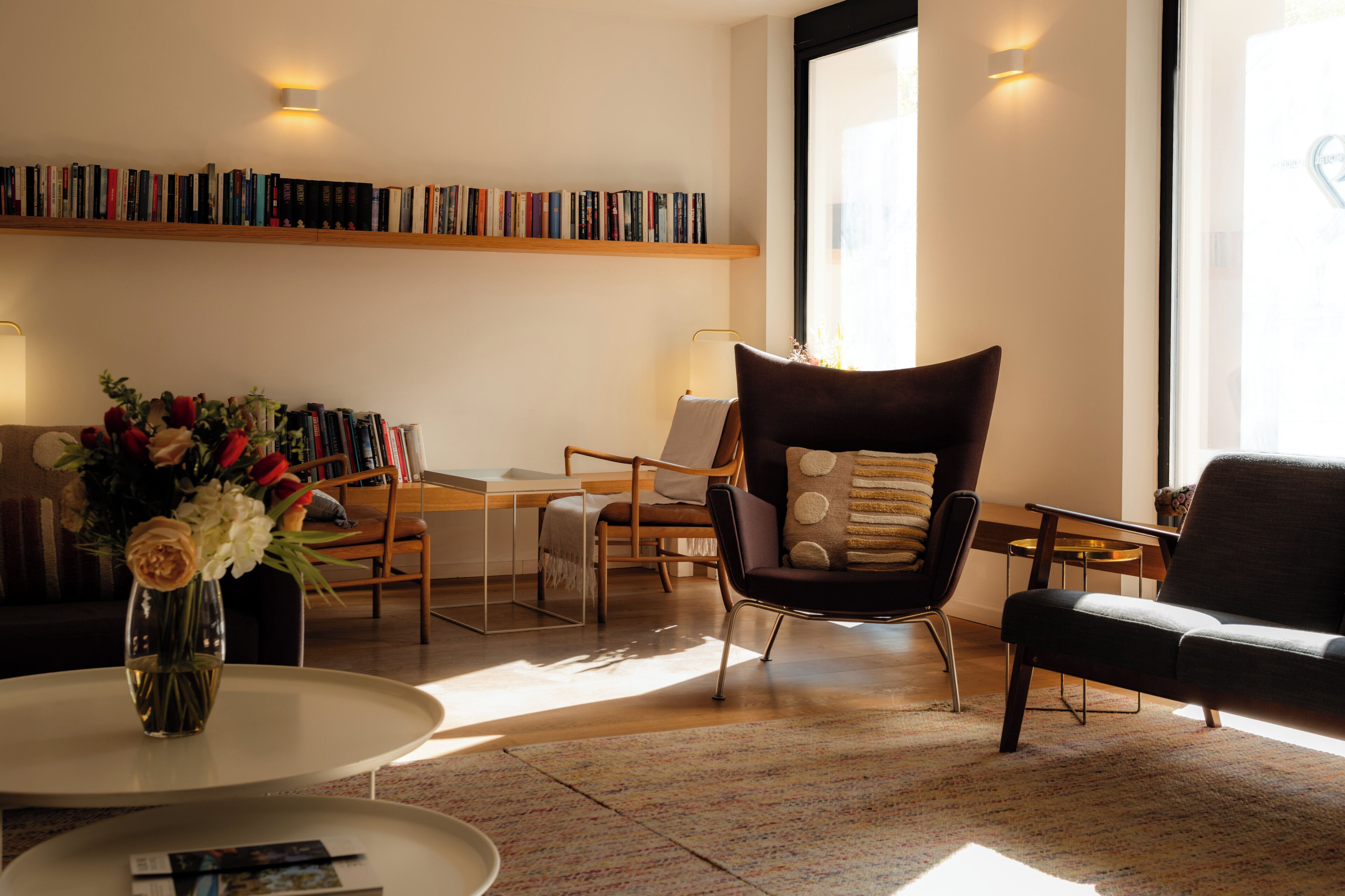 Un salon moderne avec une bibliothèque, une table basse ornée d’un vase de fleurs et deux fauteuils.