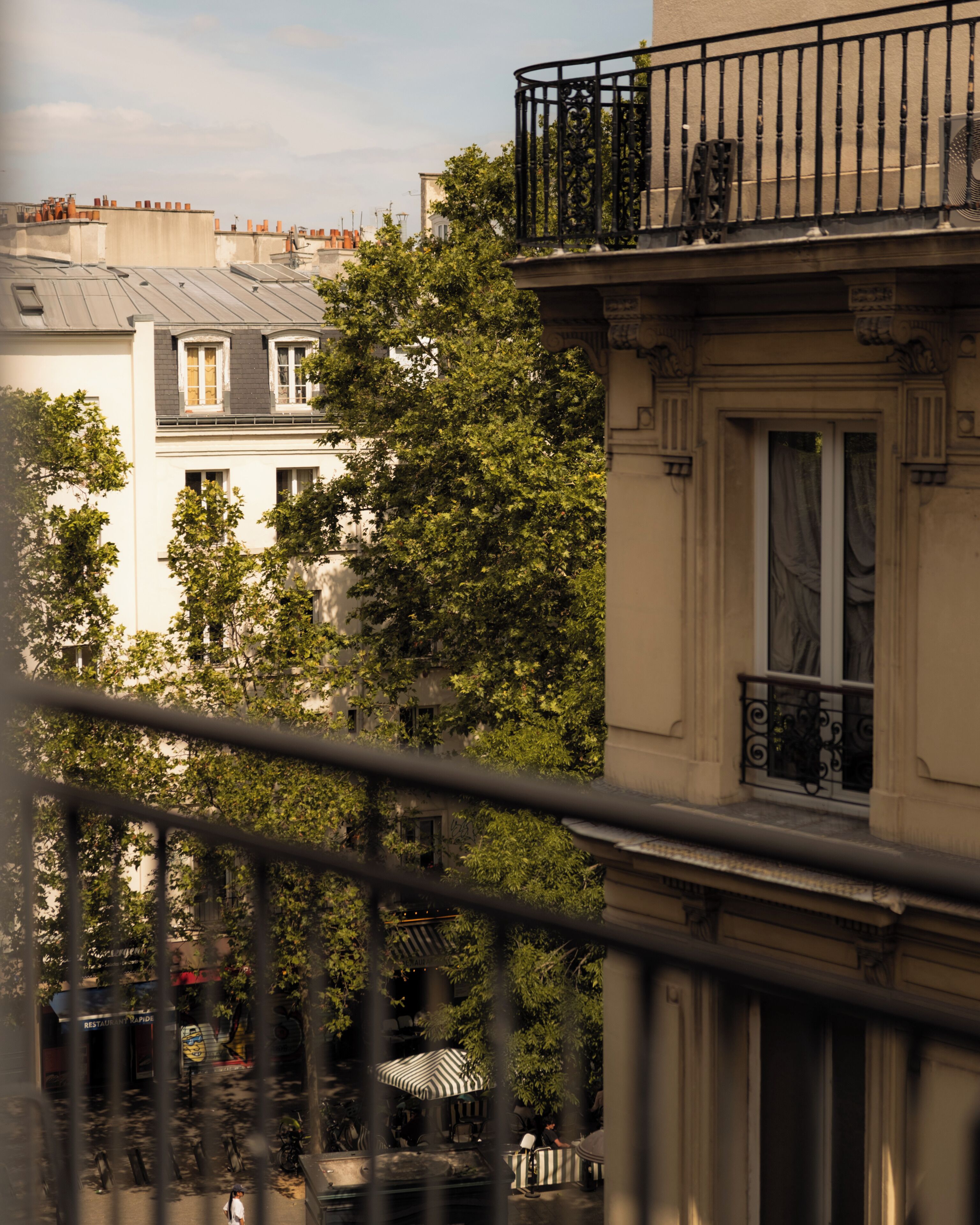 A balcony with a wrought iron railing overlooking a street with buildings and trees.