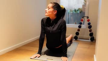 A person on a yoga mat in a room with a wooden floor and a window.