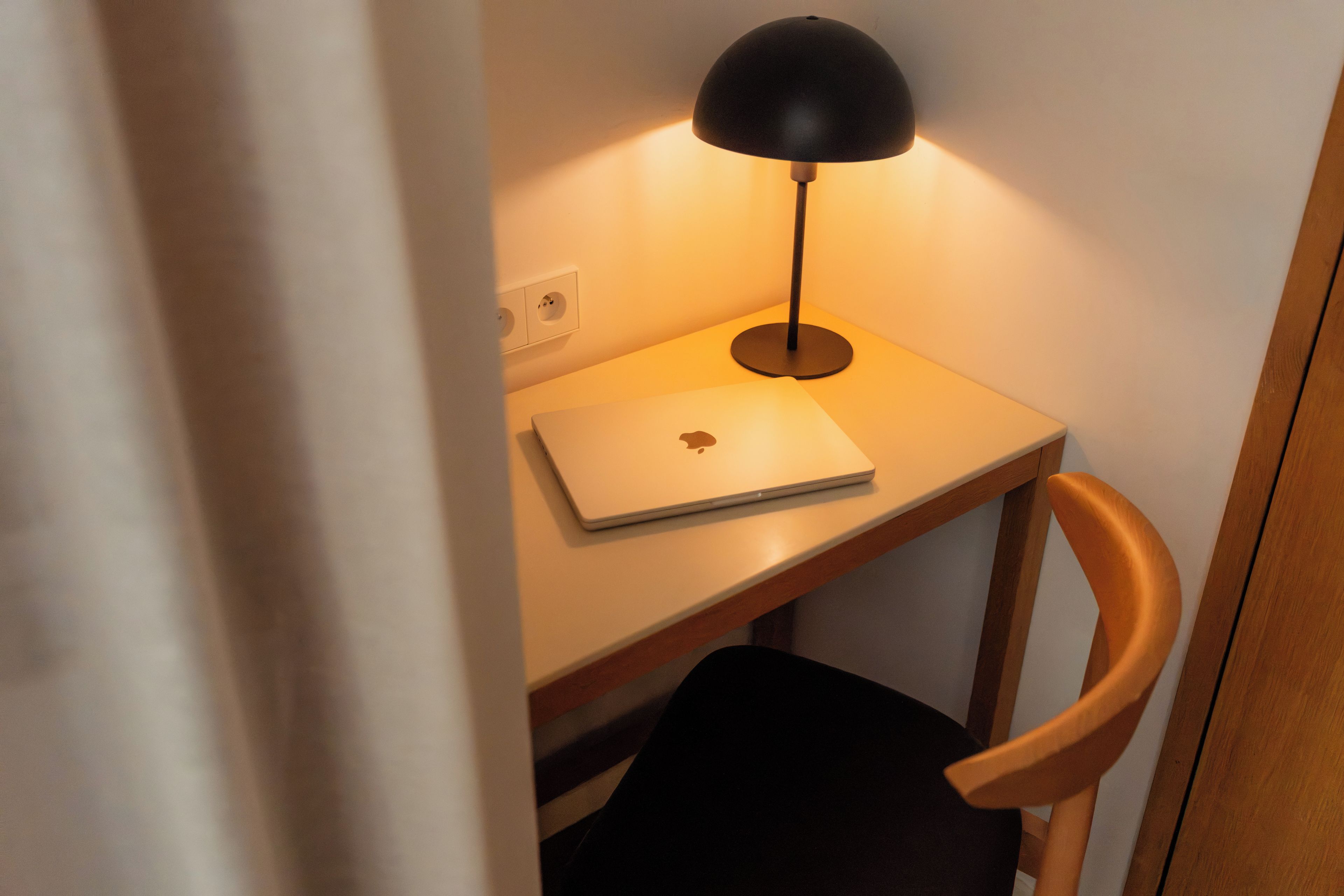 A laptop on a desk with a lamp, a chair, and a power outlet.
