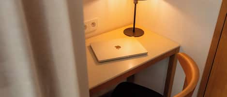 Una laptop sobre un escritorio con una lámpara, una silla y un enchufe.