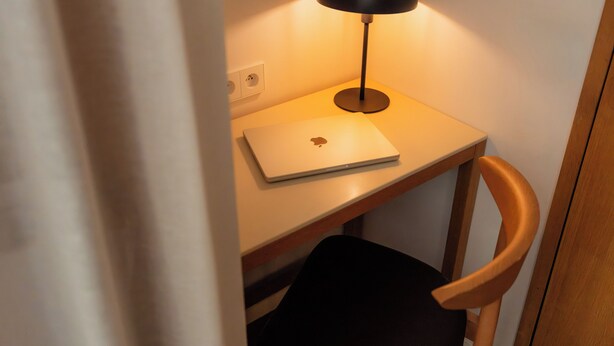 Una laptop sobre un escritorio con una lámpara, una silla y un enchufe.