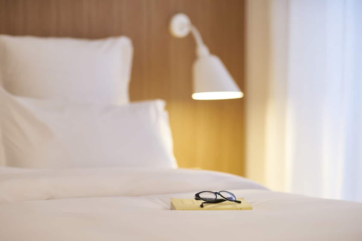 A bed with white bedding, a pair of glasses, and a book on it.