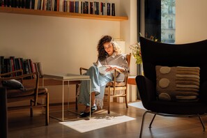 A person seated in a modern chair with a laptop, surrounded by bookshelves and a window with a view.