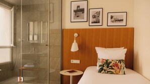 A hotel room with a glass shower enclosure, a wooden headboard, a bedside table with a book, and three framed photographs on the wall. - 9Hotel Republique (Paris)