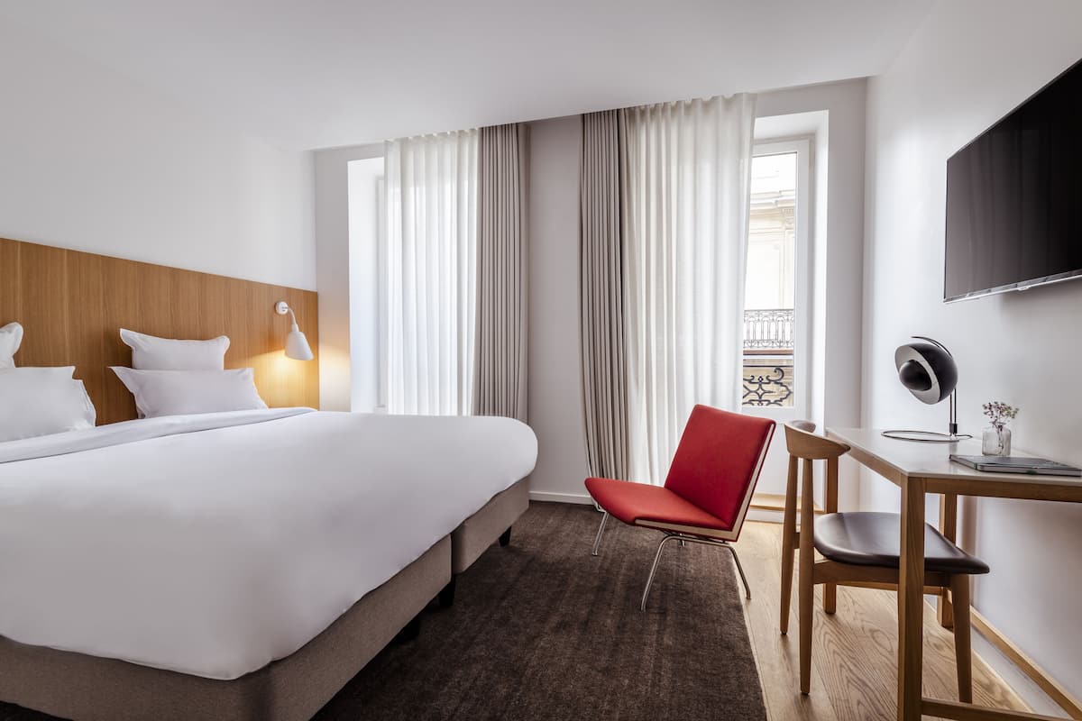 A hotel room with a large bed, a desk with a chair, a TV, and a window with curtains.