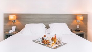 Quarto de hotel com cama, duas mesas de cabeceira, bandeja com itens de café da manhã e duas luminárias de parede.