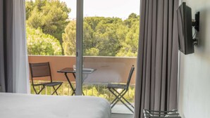 Quarto de hotel com varanda, uma cama, uma televisão e uma mesa com cadeiras.