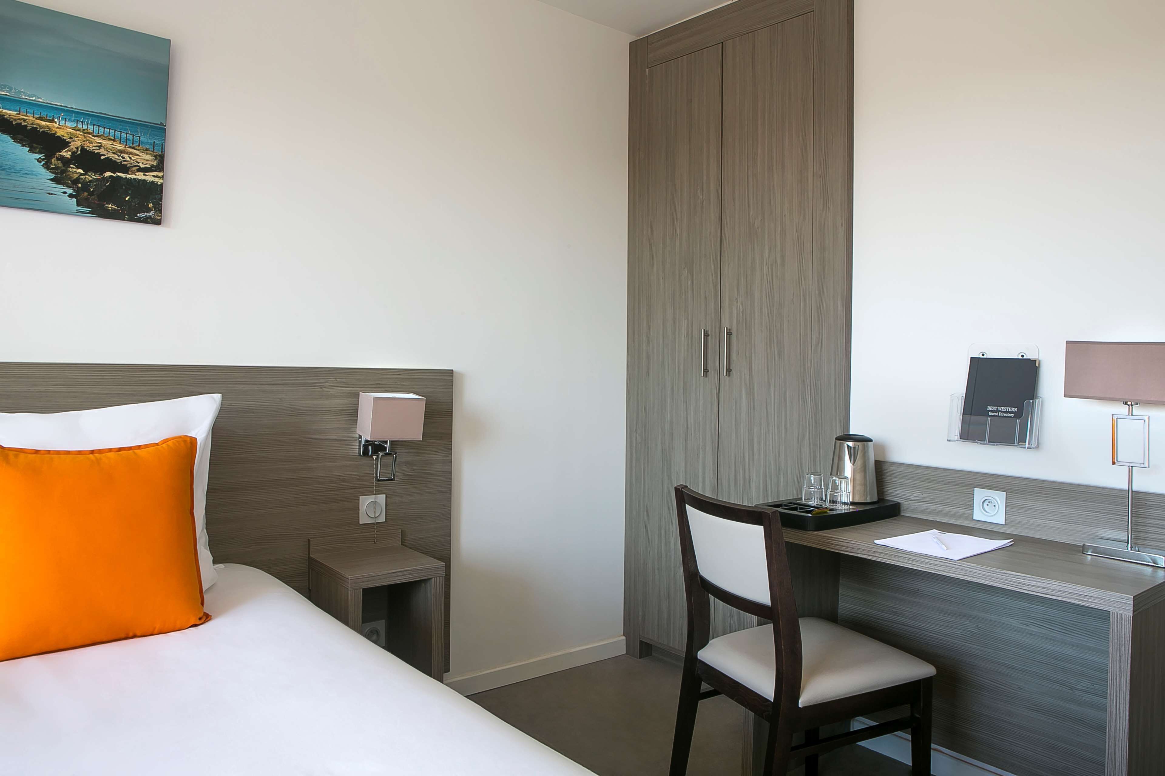 Habitación de hotel con cama, escritorio, silla, mesita de noche, lámpara, cafetera y vista al mar.