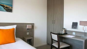 Habitación de hotel con cama, escritorio, silla, mesita de noche, lámpara, cafetera y vista al mar.