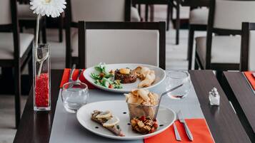 A dining table with plates of food, cutlery, and a glass of water.