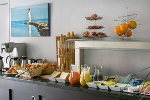Un bufé de desayuno con pan, bollería, fruta y bebidas.