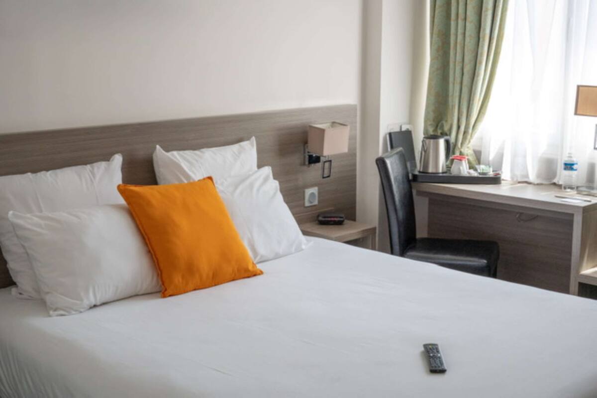 Une chambre d’hôtel avec un lit, un bureau, une chaise, une table de chevet et une fenêtre avec des rideaux.