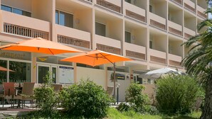Um hotel com vários andares, varandas, área de estar externa com guarda-sóis laranja e um restaurante chamado "Lamparo".