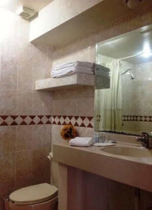 Une salle de bain avec des toilettes, un lavabo et un miroir. Il y a un porte-serviettes au-dessus du lavabo et une fleur sur le comptoir.