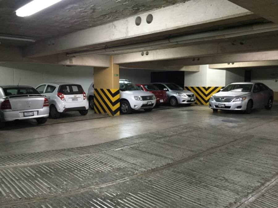 A parking garage with several cars parked in rows, concrete pillars, and chevron-patterned safety markings on the walls.