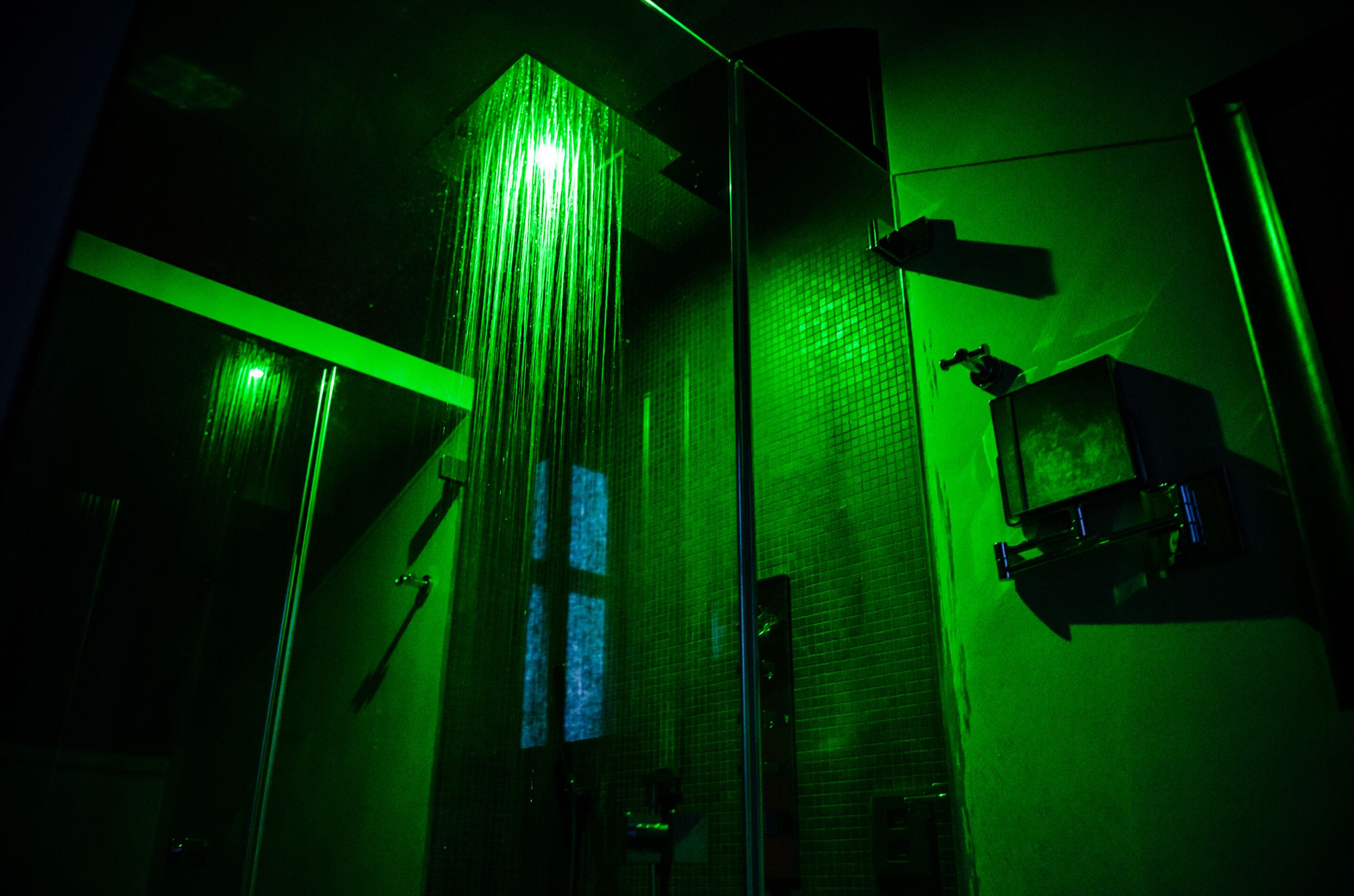 A bathroom with a glass shower enclosure, a mirror, and a green-lit wall.
