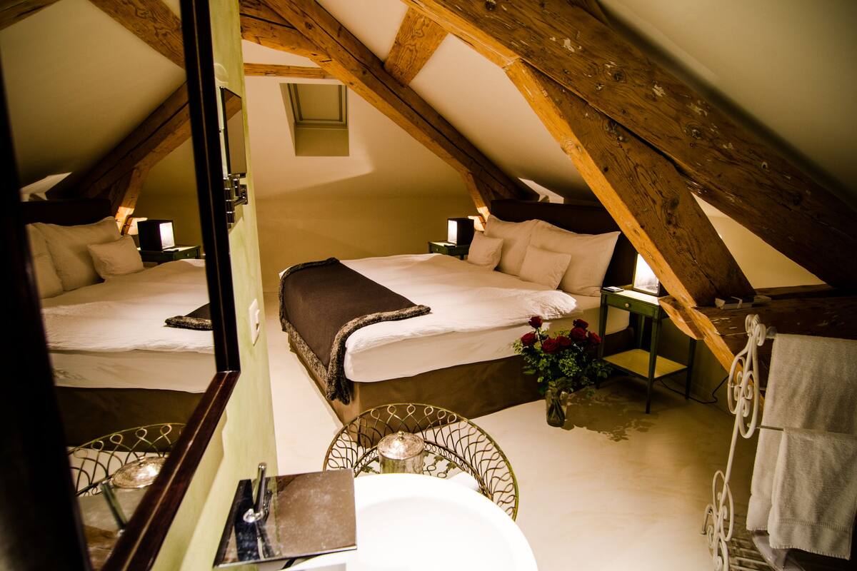 A cozy attic bedroom with two beds, a small table with a lamp, and a mirror.
