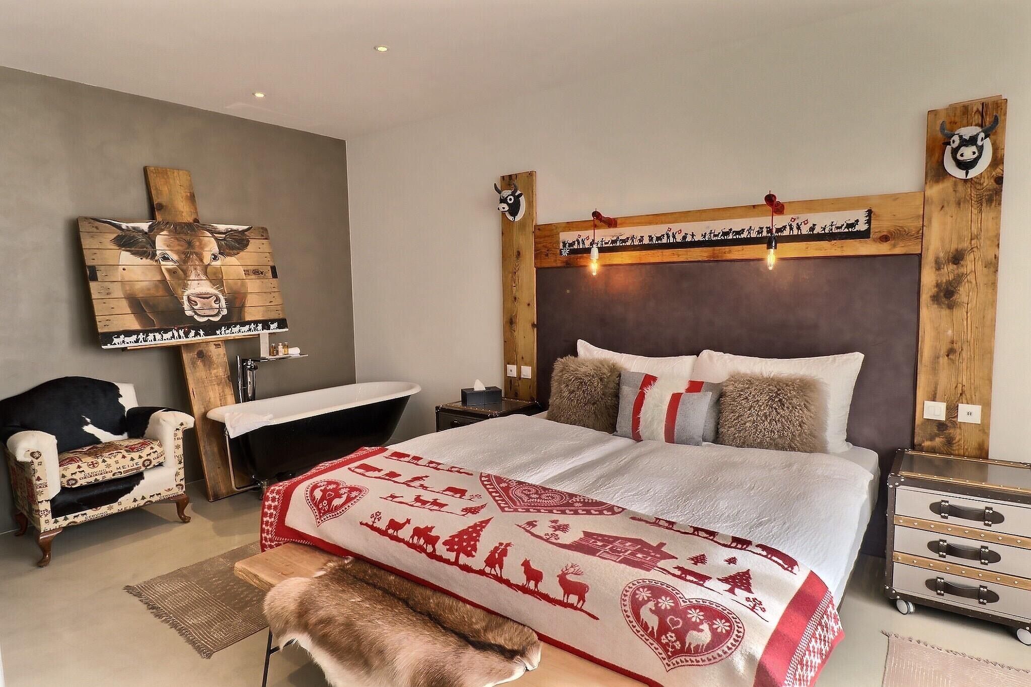 Um quarto com uma cama grande, cabeceira de madeira, mesa de cabeceira, uma cadeira, um banco e uma cômoda.