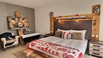 Um quarto com uma cama grande, cabeceira de madeira, mesa de cabeceira, uma cadeira, um banco e uma cômoda.