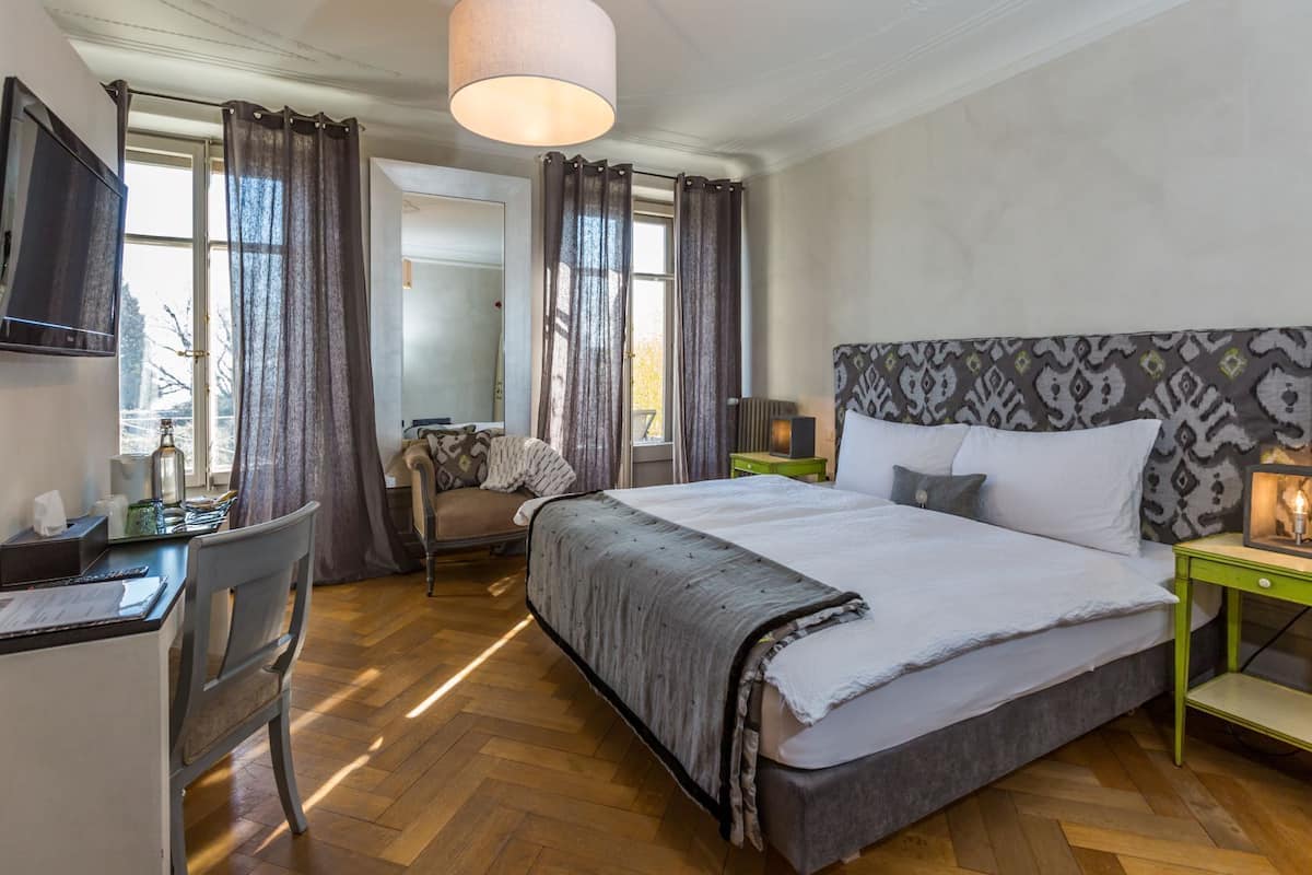 A hotel room with a large bed, a desk with a chair, a TV, and a window with curtains.