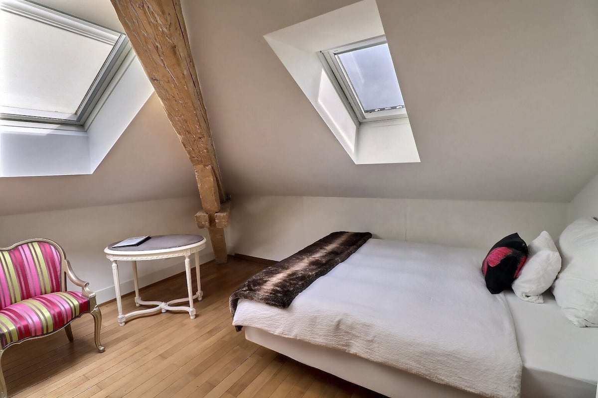 A bedroom with a bed, a chair, a small table, and two skylights.