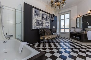 Un baño con suelo a cuadros, una bañera, un box de ducha de vidrio, una cebra montada en la pared y un candelabro.