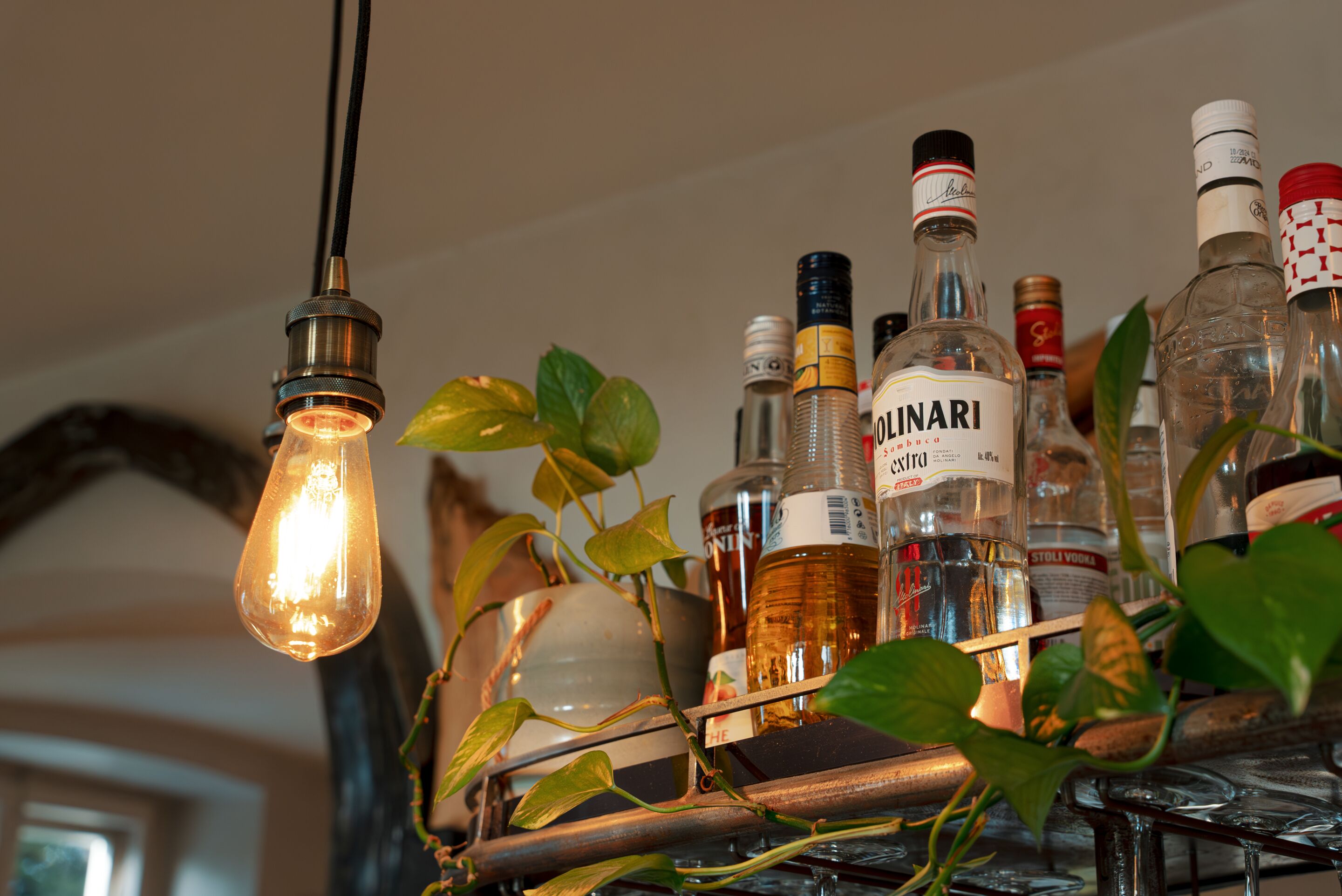 Una balda amb diverses ampolles de licor i una làmpada penjant.