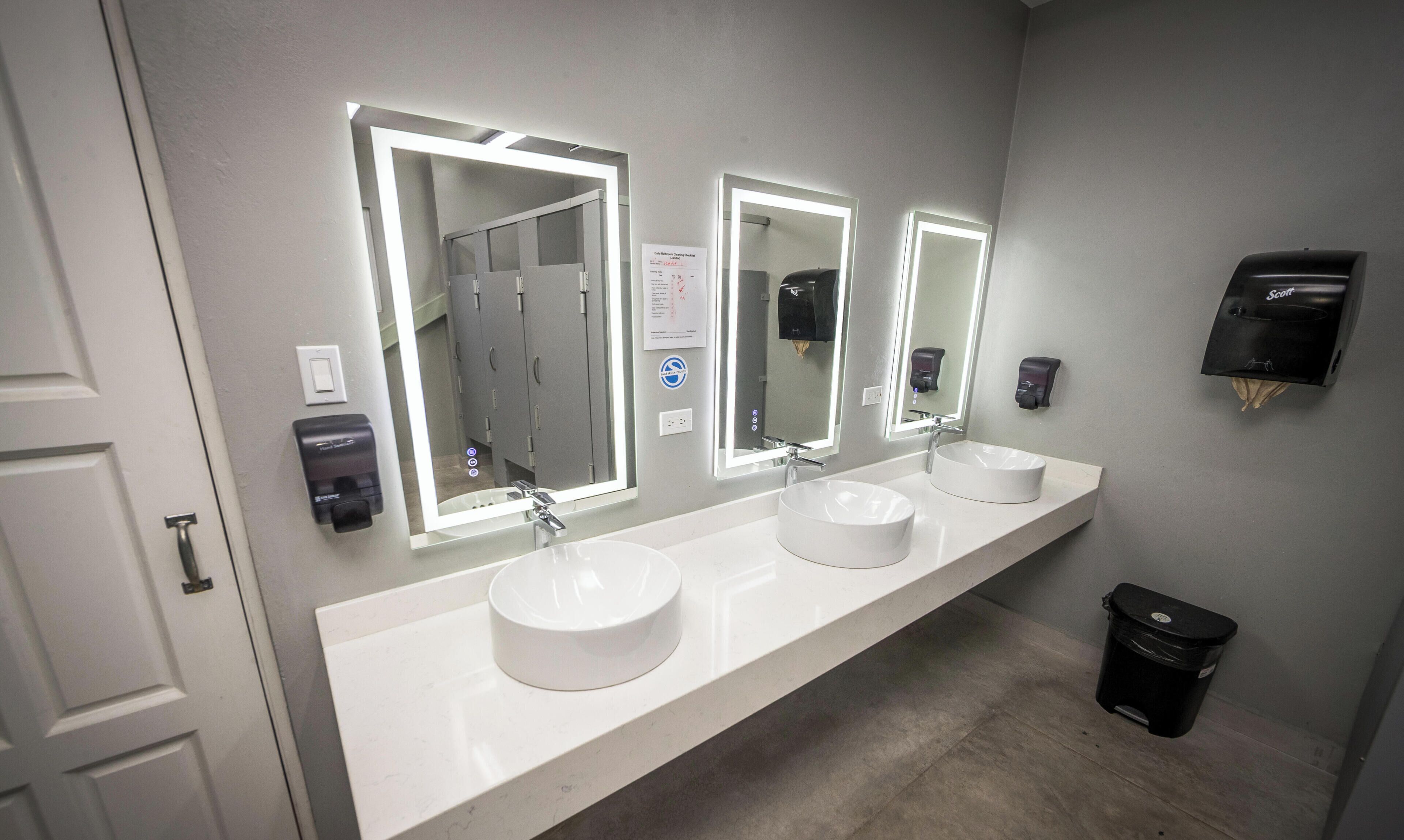 Une salle de bain avec trois lavabos, des miroirs et des sèche-mains.