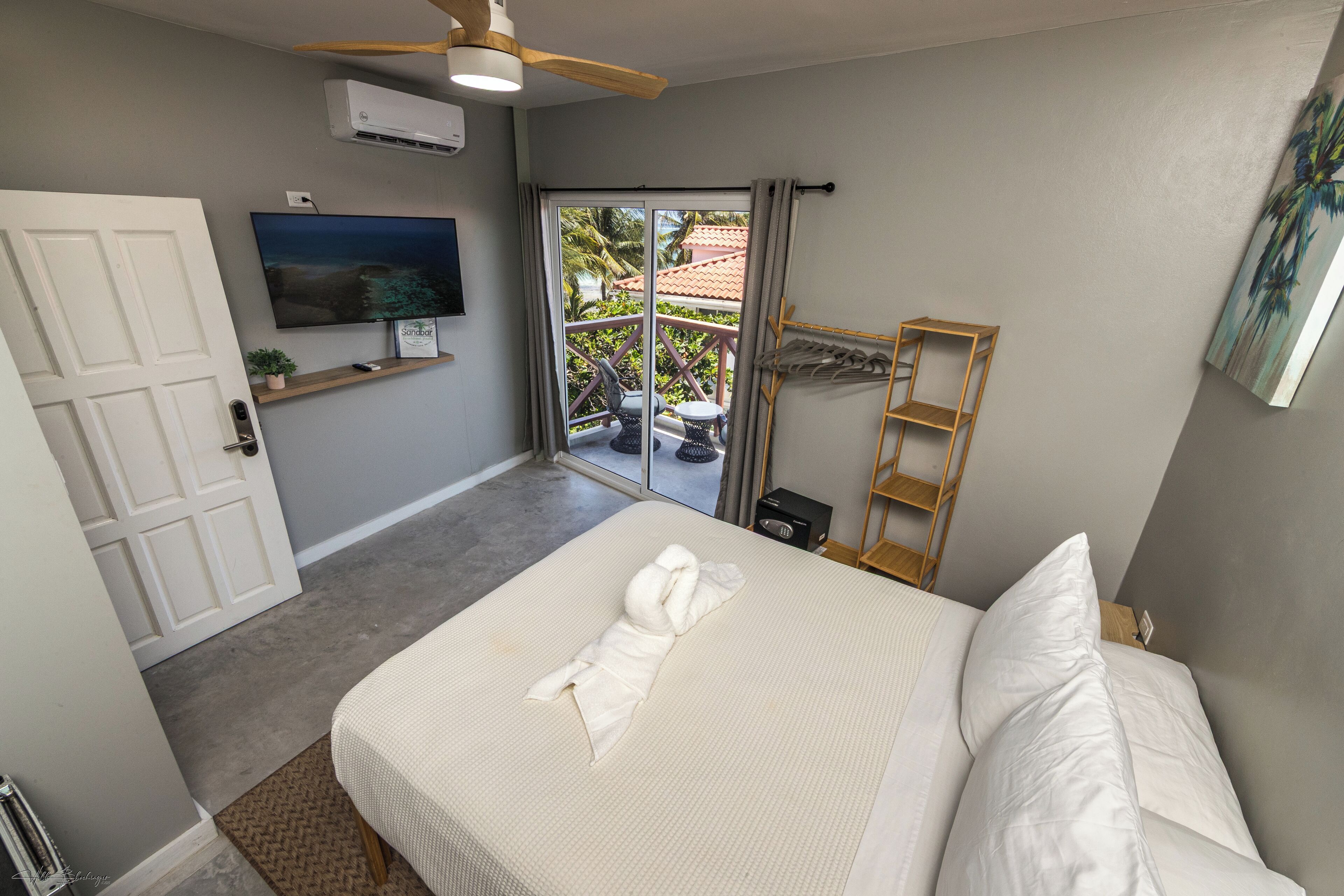 A hotel room with a bed, a television, a sliding glass door to an outdoor area, and a ceiling fan.