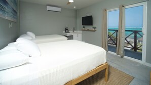 Un dormitorio con dos camas, ventilador de techo, televisor y balcón con vista al océano.