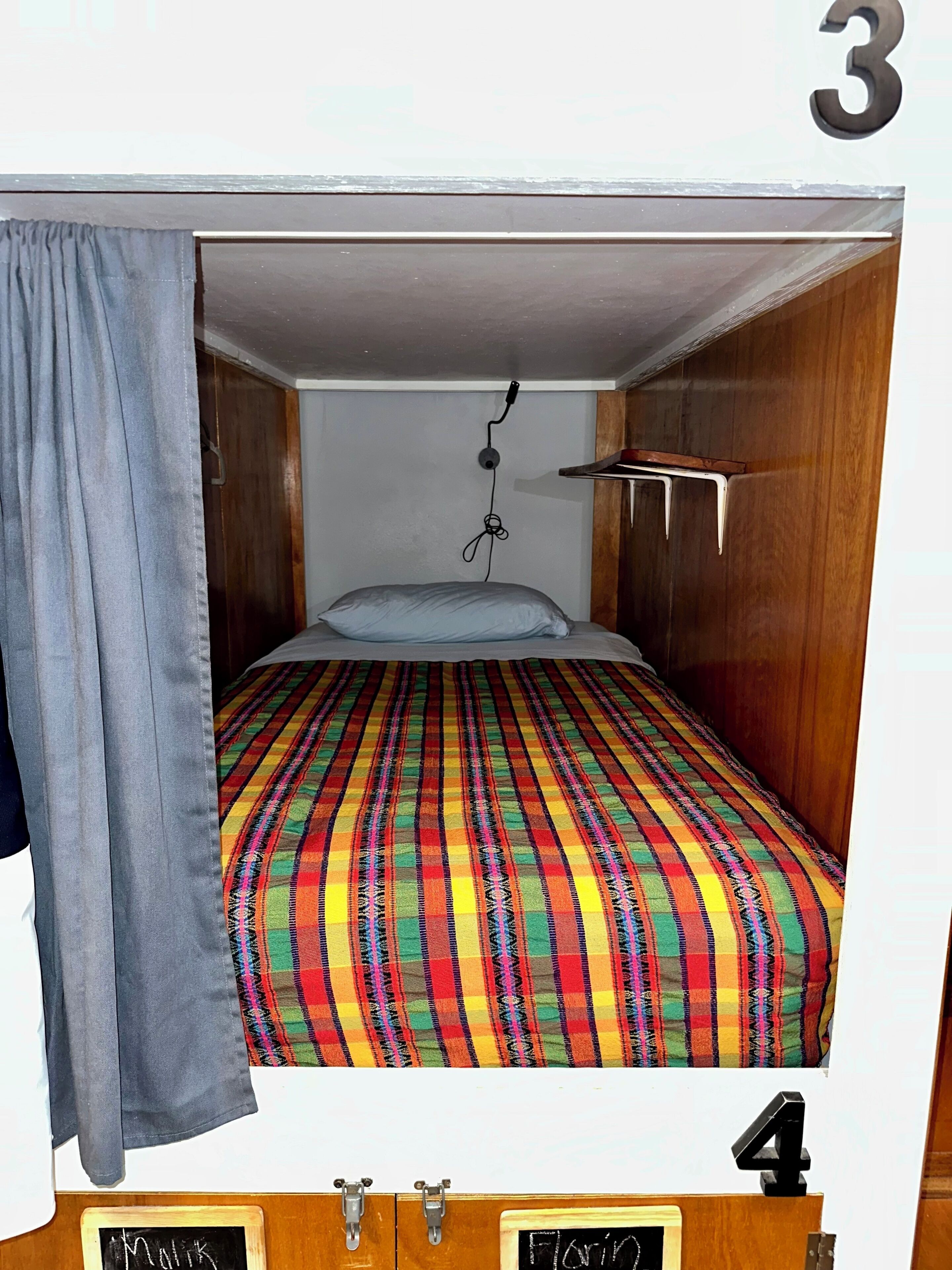A bunk bed with a colorful striped bedspread, a hanging phone, and a small shelf.
