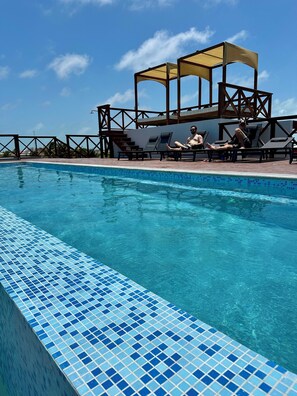 Una piscina con bordes de azulejos, sillas de descanso y un área de estar cubierta.
