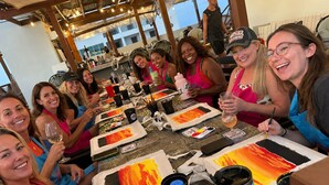 Un grupo de personas sentadas alrededor de una mesa con materiales de arte y pintura.