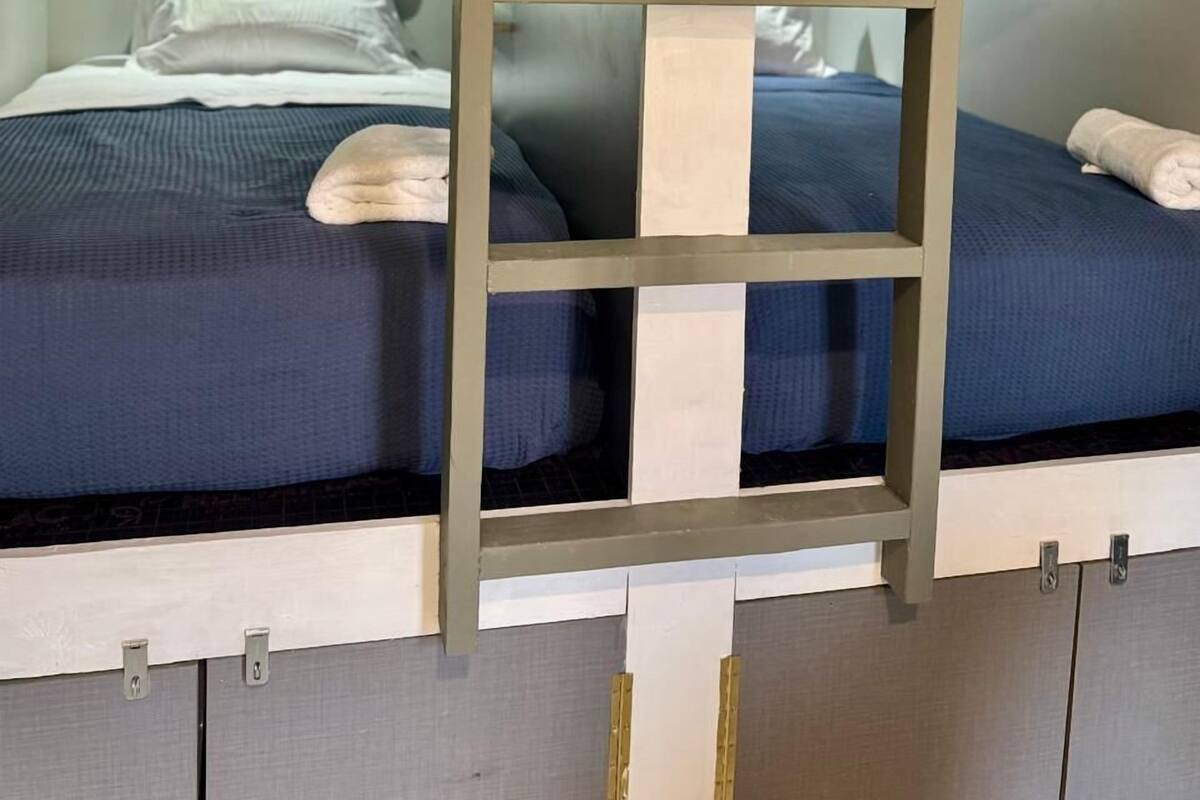 A bunk bed room with a ladder in the center, white handles on the beds, and a white pillow on the lower bunk.