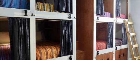 Habitación tipo dormitorio con literas, puertas numeradas y una escalera de madera.