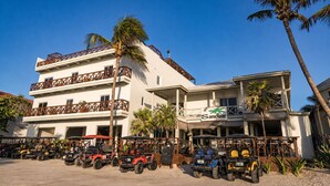 Un hotel de varios pisos con un bar de playa llamado 'Sandbar', que cuenta con una fila de carros de golf en la parte delantera.