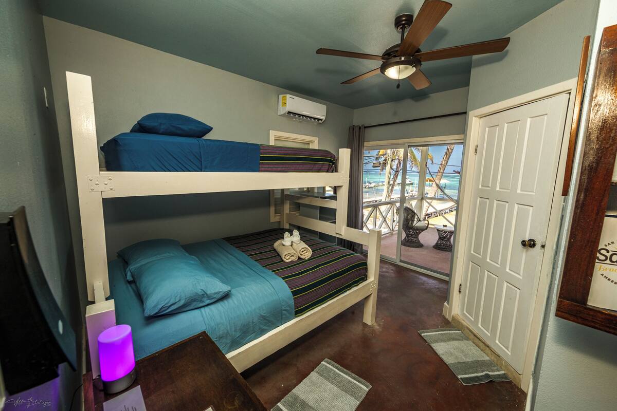A bunk bed room with a ceiling fan, an air conditioning unit, and a view of the beach through the door.