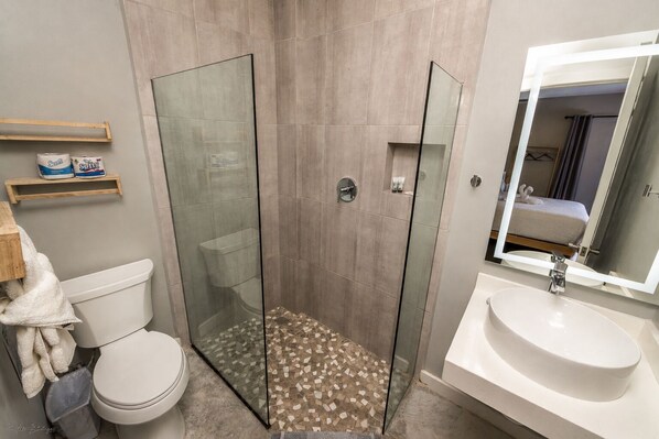 A bathroom with a glass-enclosed shower, a toilet, a sink, and a mirror. - Sandbar Beachfront Hotel & Hostel (San Pedro)