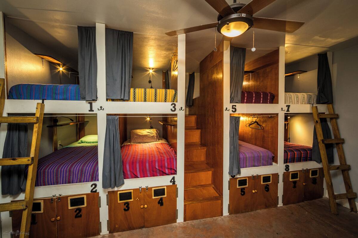 A multi-level bunk bed room with wooden bunk beds, a central staircase, and a ceiling fan.