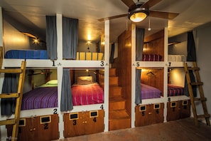 Habitación con literas de madera a varios niveles, una escalera central y un ventilador de techo.